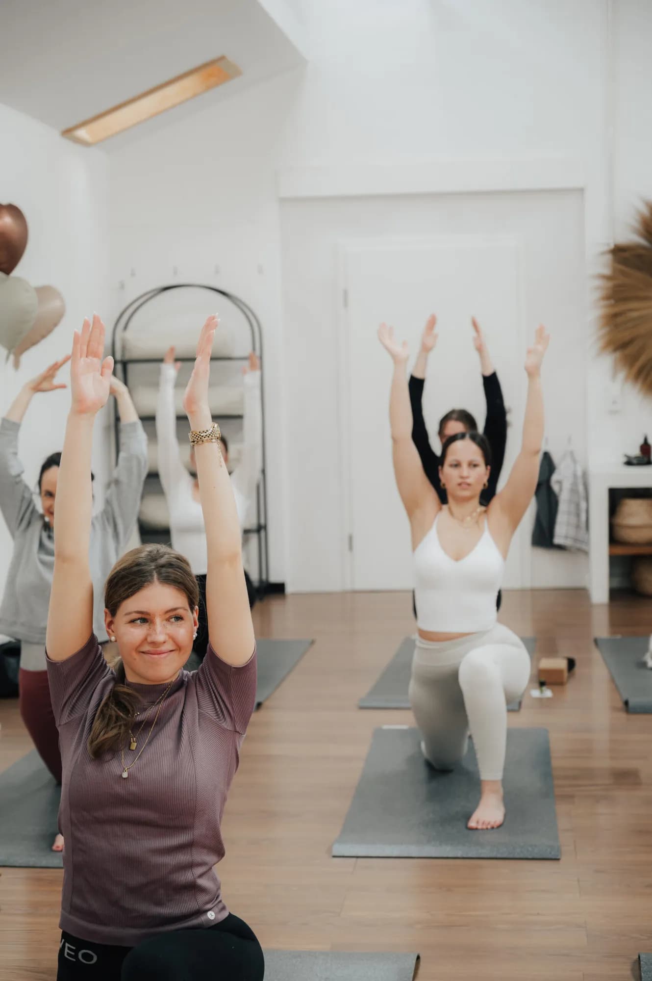 Lächelnde Teilnehmerin mit erhobenen Armen in einer Yogaklasse im Studio La Soulis
